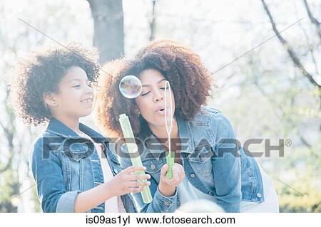 Stock Image - Mother and daughter blowing bubbles together. Fotosearch