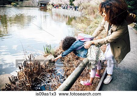 Mother gripping daughter stretching over guard rail to touch plant View Large Photo Image Stock Image - Mother gripping daughter stretching over guard rail to touch plant. Fotosearch
