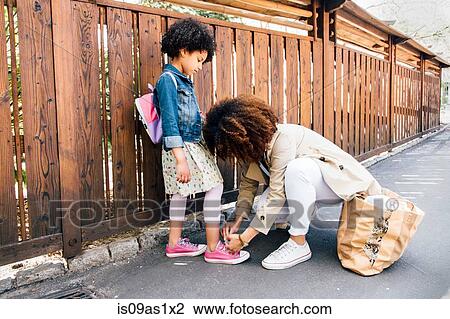 Mother kneeling by fence tying daughters shoelace View Large Photo Image Stock Image - Mother kneeling by fence tying daughters shoelace. Fotosearch