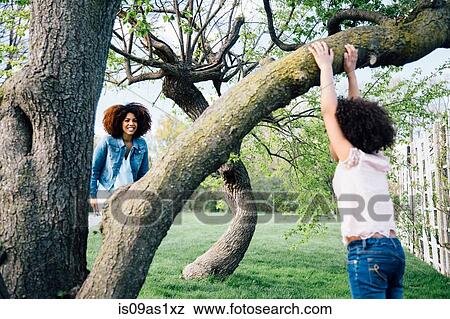 Stock Photo - Mother smiling at daughter climbing tree. Fotosearch