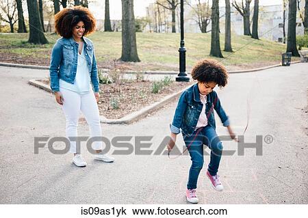 Mother watching daughter using skipping rope on pathway, smiling View Large Photo Image Stock Image - Mother watching daughter using skipping rope on pathway, smiling. Fotosearch