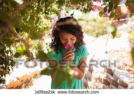 Stock Image - Portrait of girl in garden smelling pink blossom. Fotosearch