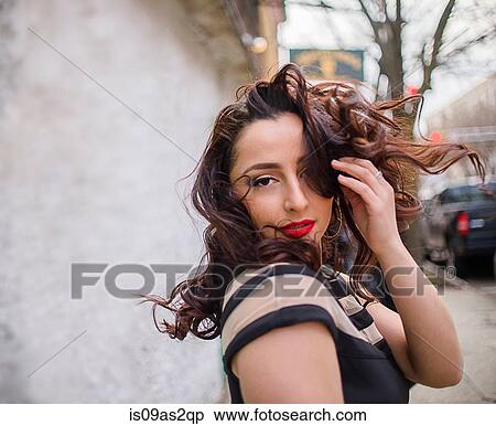 Stock Photography - Portrait of glamorous young woman with hand in hair on sidewalk. Fotosearch