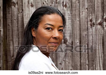 Stock Image - Portrait of mature woman looking over her shoulder in front of garden fence. Fotosearch