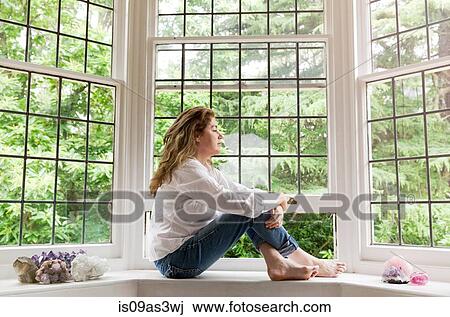 Portrait of mature woman sitting on living room windowsill looking out of window View Large Photo Image Stock Image - Portrait of mature woman sitting on living room windowsill looking out of window. Fotosearch