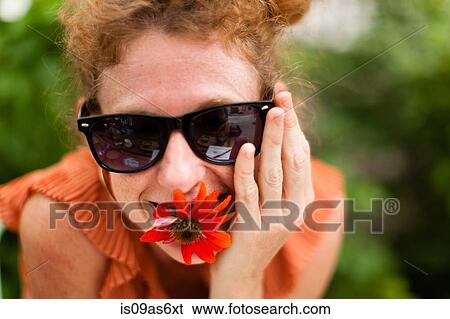 Stock Photograph - Portrait of mid adult woman with red flower in her mouth. Fotosearch