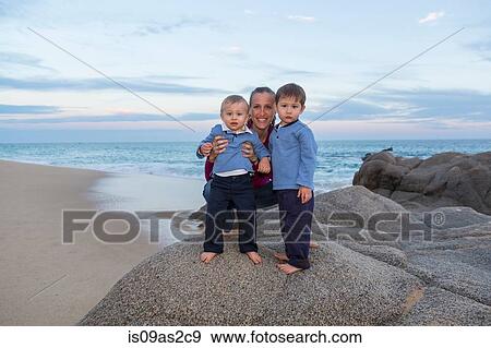 Stock Photo - Portrait of mother and sons on rocks on beach. Fotosearch
