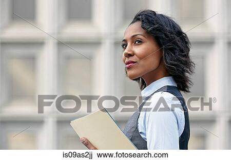 Stock Image - Portrait of young business woman holding paper work, looking away, side view. Fotosearch