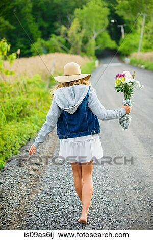 Rear view of bare footed young woman walking on rural gravel road carrying bunch of flowers View Large Photo Image Stock Image - Rear view of bare footed young woman walking on rural gravel road carrying bunch of flowers. Fotosearch