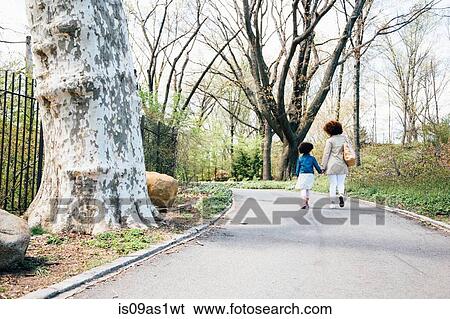 Rear view of mother and daughter walking along pathway holding hands View Large Photo Image Stock Photograph - Rear view of mother and daughter walking along pathway holding hands. Fotosearch