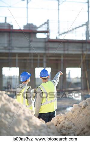 Stock Photo - Rear view of surveyor and builder on construction site. Fotosearch