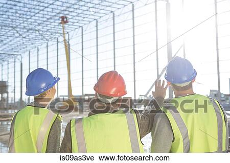 Stock Image - Rear view of surveyor and builders meeting on construction site. Fotosearch