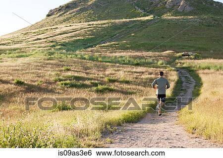 Stock Photograph - Rear view of young male runner running up hillside track. Fotosearch