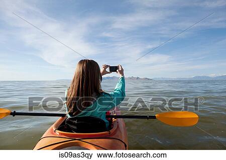 Stock Photo - Rear view of young woman in kayak taking photograph, Great Salt Lake, Utah, USA. Fotosearch