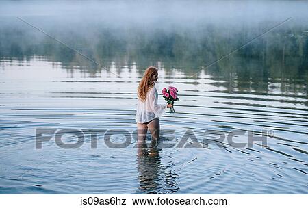 Rear view of young woman wading in misty lake holding bunch of pink roses View Large Photo Image Stock Photo - Rear view of young woman wading in misty lake holding bunch of pink roses. Fotosearch