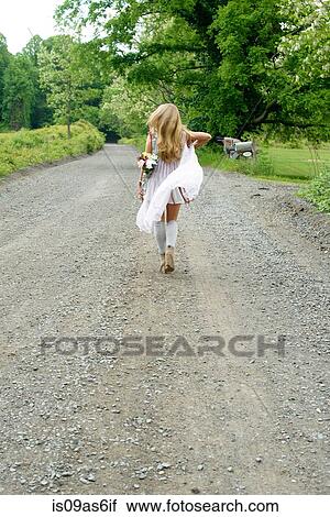 Rear view of young woman walking on rural road with flowers behind her back View Large Photo Image Stock Image - Rear view of young woman walking on rural road with flowers behind her back. Fotosearch