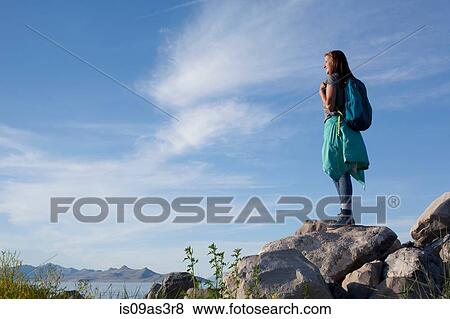 Stock Photo - Rear view of young woman wearing backpack standing on rocks looking away, Great Salt Lake, Utah, USA. Fotosearch