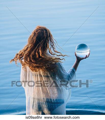 Rear view of young woman with long red hair standing in lake holding crystal ball View Large Photo Image Stock Photography - Rear view of young woman with long red hair standing in lake holding crystal ball. Fotosearch