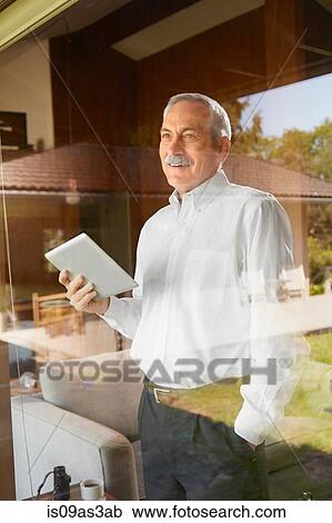 Stock Image - Senior man at home, holding digital tablet. Fotosearch