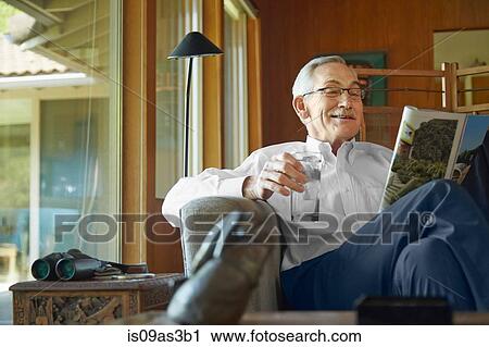 Stock Image - Senior man at home, reading magazine. Fotosearch