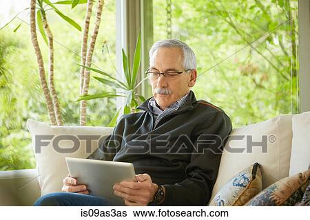 Stock Photograph - Senior man at home, using digital tablet. Fotosearch