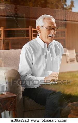 Stock Image - Senior man at home, using laptop. Fotosearch