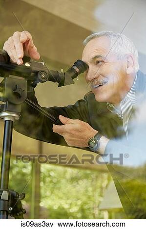 Stock Photo - Senior man at home, using telescope through window. Fotosearch