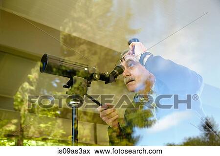 Stock Photo - Senior man at home, using telescope through window. Fotosearch