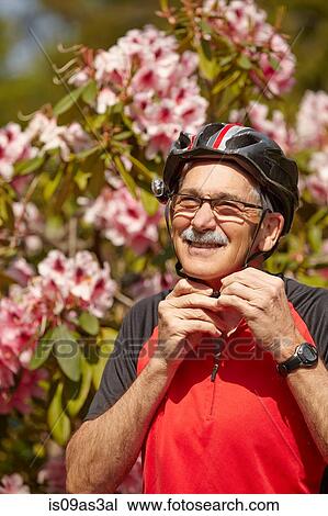Stock Image - Senior man putting on cycle helmet. Fotosearch