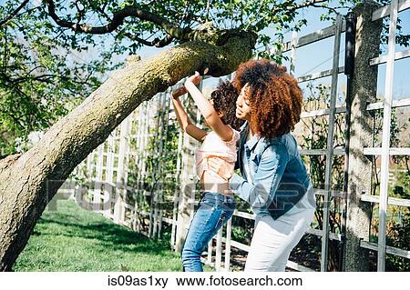 Stock Photo - Side view of mother helping daughter to climb tree. Fotosearch