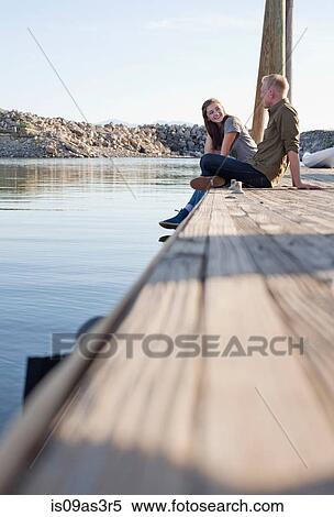Stock Photography - Side view of young couple sitting on wooden pier talking, Great Salt Lake, Utah, USA. Fotosearch
