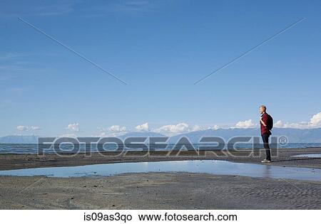 Side view of young man standing at waters edge looking out, Great Salt lake, Utah, USA View Large Photo Image Picture - Side view of young man standing at waters edge looking out, Great Salt lake, Utah, USA. Fotosearch