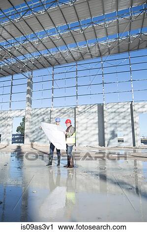 Stock Image - Surveyor and architect on construction site looking at blueprint. Fotosearch