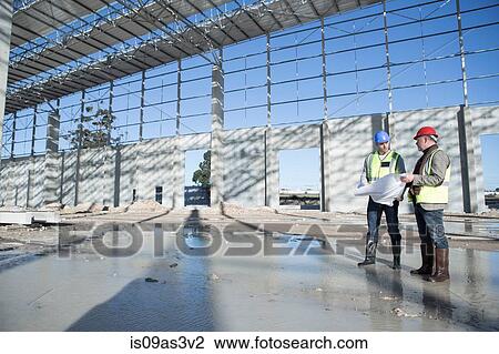 Stock Image - Surveyor and architect on construction site discussing blueprint. Fotosearch