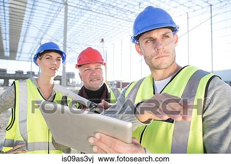 Stock Image - Surveyor and architects using digital tablet on construction site. Fotosearch