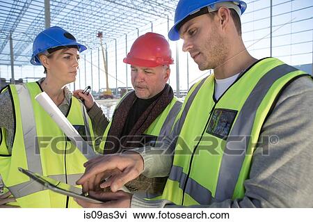 Stock Image - Surveyor and builders using digital tablet on construction site. Fotosearch