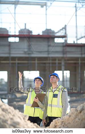 Stock Photo - Surveyor looking up whilst talking to builder on construction site. Fotosearch