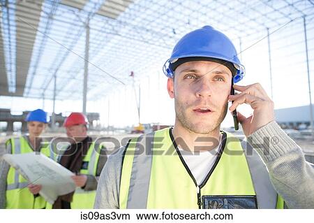 Picture - Surveyor talking on smartphone on construction site. Fotosearch