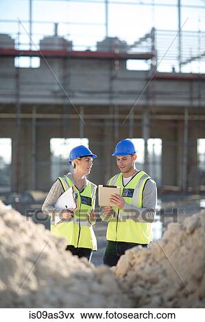 Stock Photo - Surveyor using digital tablet talking to builder on construction site. Fotosearch