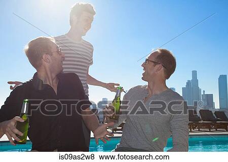 Stock Photo - Three adult male friends drinking beers at rooftop bar with Los Angeles skyline, USA. Fotosearch