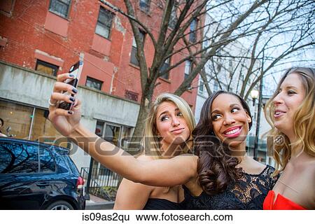 Three glamorous young adult female friends taking smartphone selfie on street View Large Photo Image Stock Photograph - Three glamorous young adult female friends taking smartphone selfie on street. Fotosearch