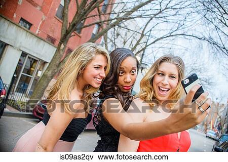 Three young adult female friends taking smartphone selfie on street View Large Photo Image Stock Photo - Three young adult female friends taking smartphone selfie on street. Fotosearch