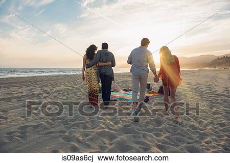 Stock Image - Two young couples walking along beach, rear view. Fotosearch