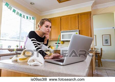 Stock Photo - Woman using laptop in kitchen. Fotosearch