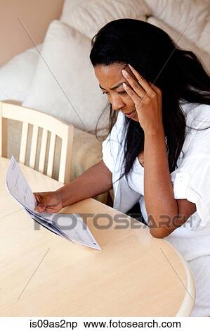 Stock Photography - Worried mature woman sitting at dining table reading bill. Fotosearch