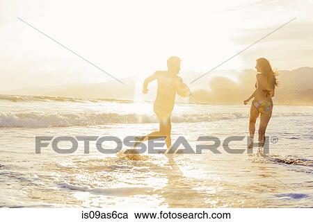 Stock Image - Young couple fooling around on beach, on sea, sunset. Fotosearch