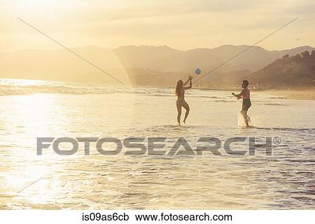 Stock Image - Young couple fooling around on beach, on sea, sunset. Fotosearch