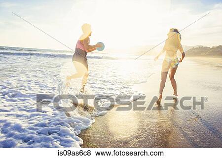 Stock Photo - Young couple fooling around on beach, on sea, sunset. Fotosearch