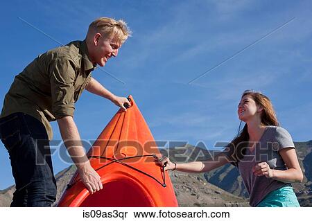 Stock Photography - Young couple preparing orange kayak, looking at each other smiling. Fotosearch