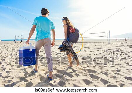 Stock Image - Young couple walking on beach, holding cool box, rear view. Fotosearch